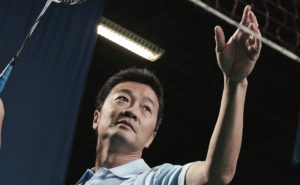 Chinese man poised to smash a badminton shuttlecock.