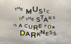 The words "the music of the stars is a cure for darkness" set against a stormy sky.